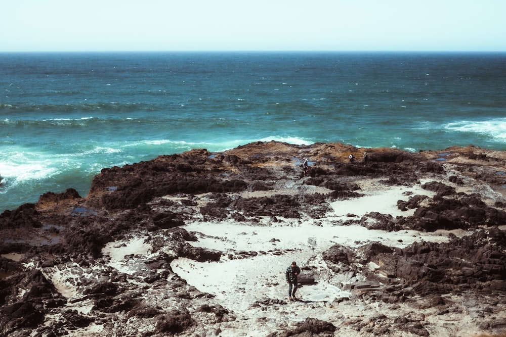um homem de pé no topo de um penhasco rochoso ao lado do oceano