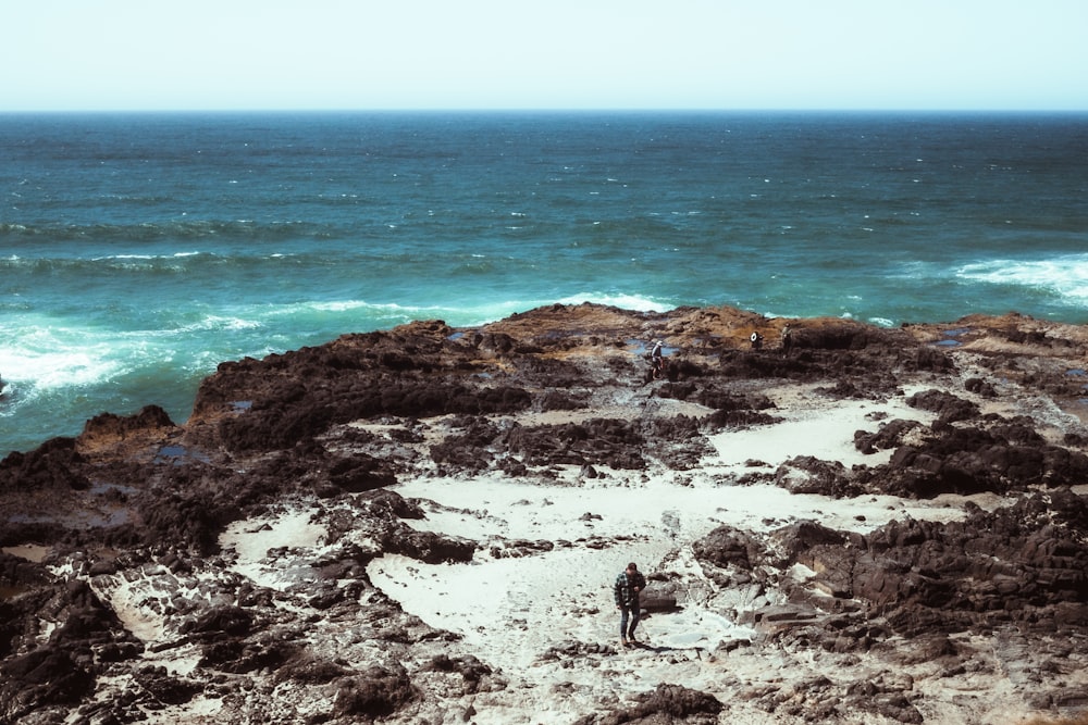 a man standing on top of a rocky cliff next to the ocean