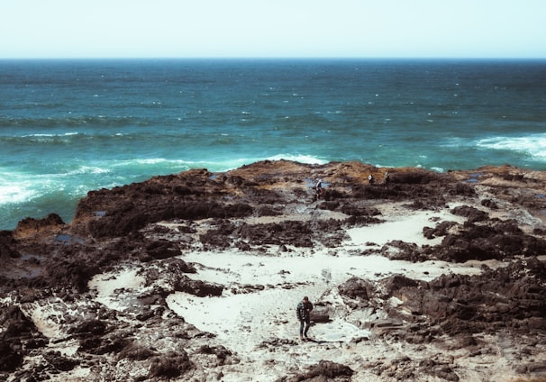 a man standing on top of a rocky cliff next to the ocean