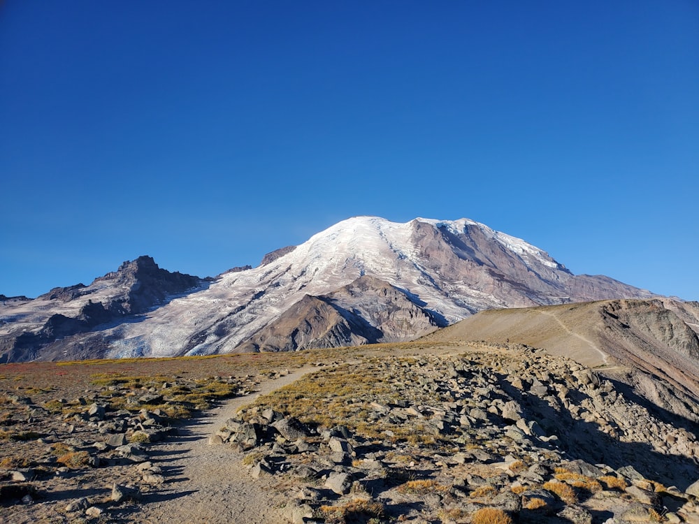 a dirt path leading to a snow covered mountain