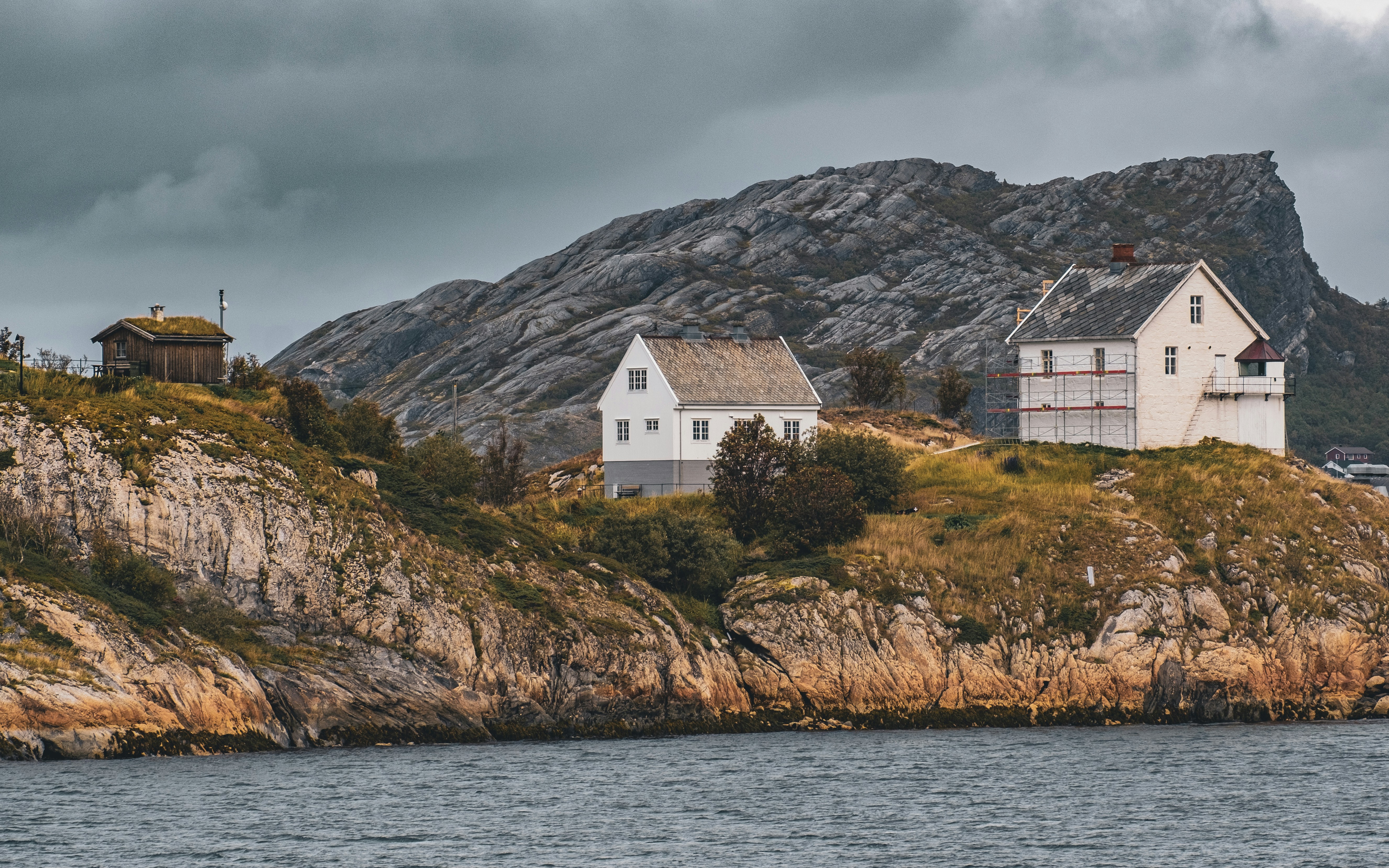 a couple of houses sitting on top of a hill next to a body of water, a tiny peninsula at the coast of Bodø