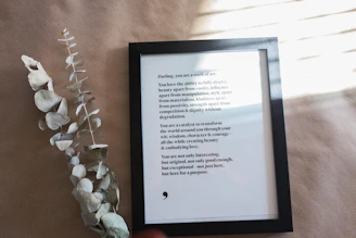 a person holding a framed book next to a plant