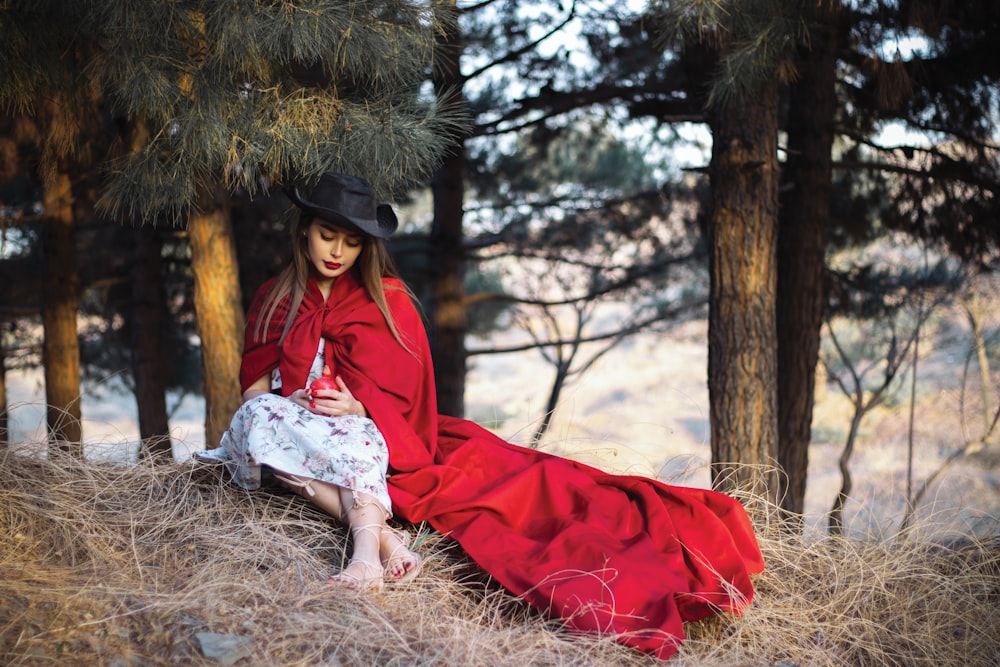 a woman in a red dress and hat sitting in the woods