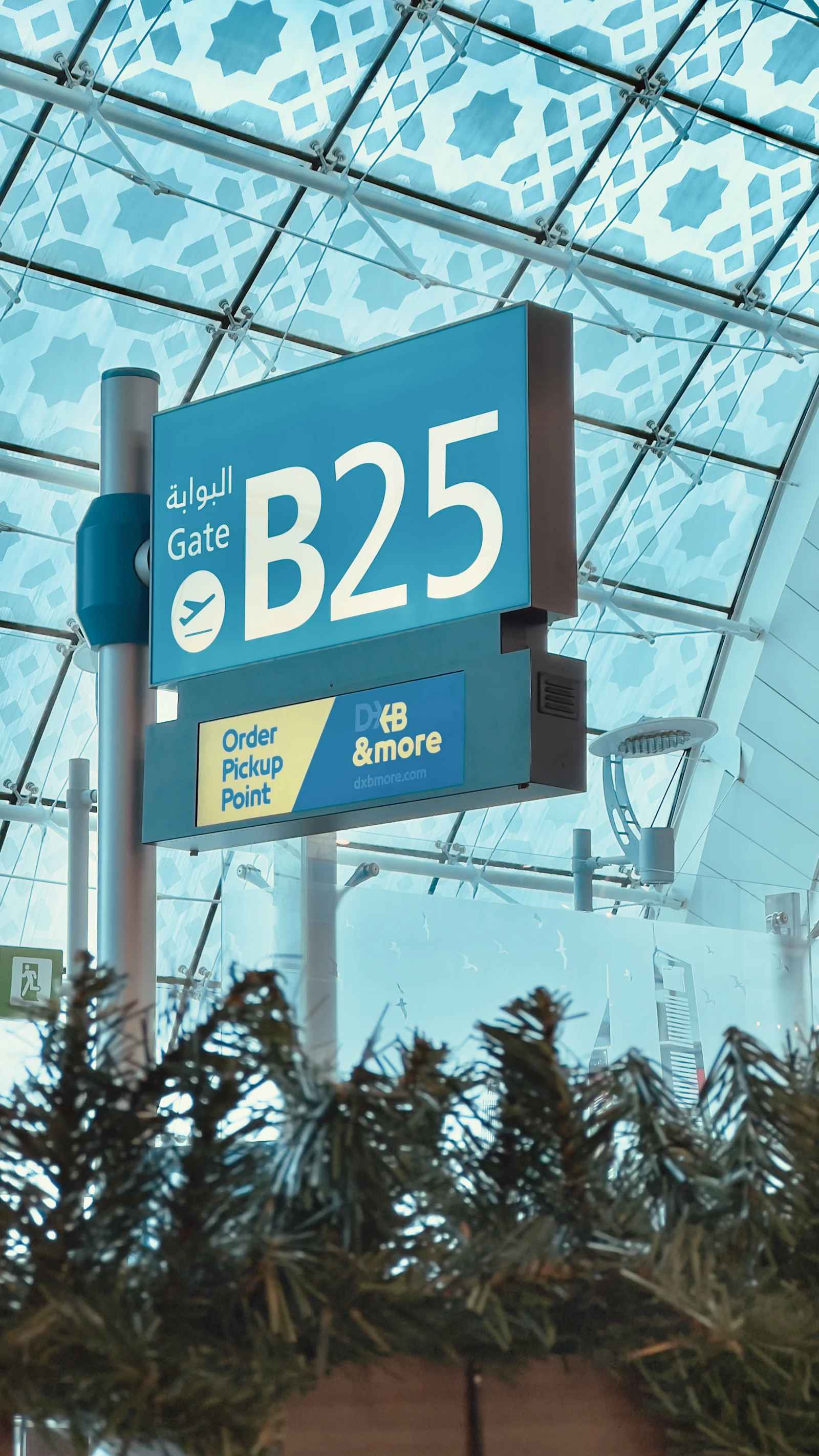 Travel photograph: A turquoise B25 gate sign hangs beneath the patterned glass roof at Dubai International Airport.