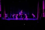 Group of four students mid-twerk choreography, bathed in cinematic purple light.