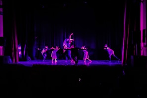 Group of four students mid-twerk choreography, bathed in cinematic purple light.