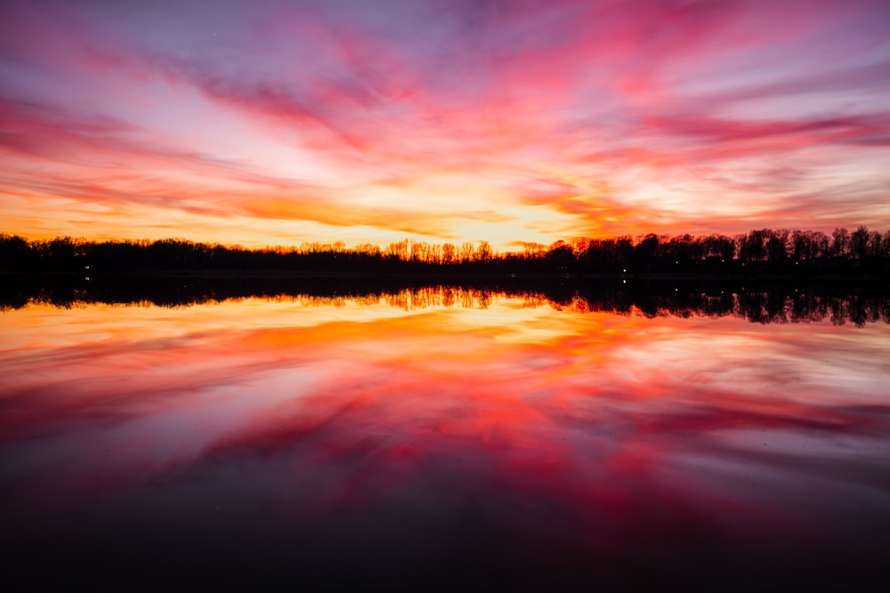 a sunset over a body of water with trees in the background