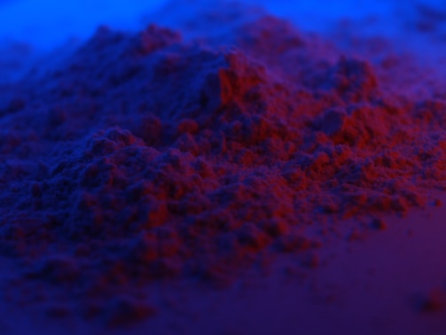A textured surface covered with a fine, powdery substance under intense red and blue lighting, creating an abstract, otherworldly appearance.
