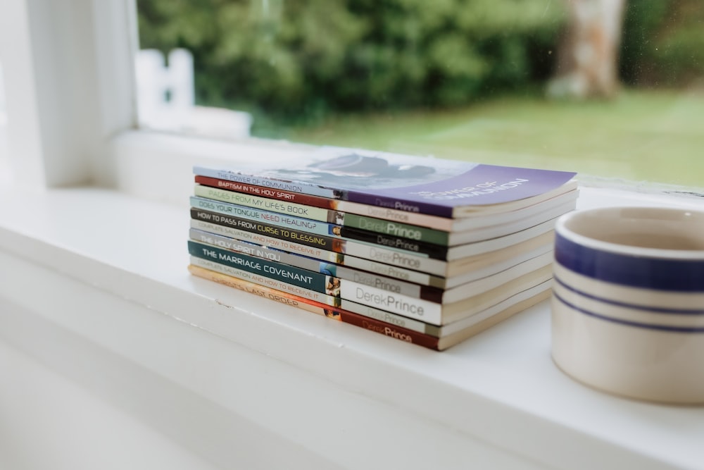 a stack of books sitting on top of a window sill