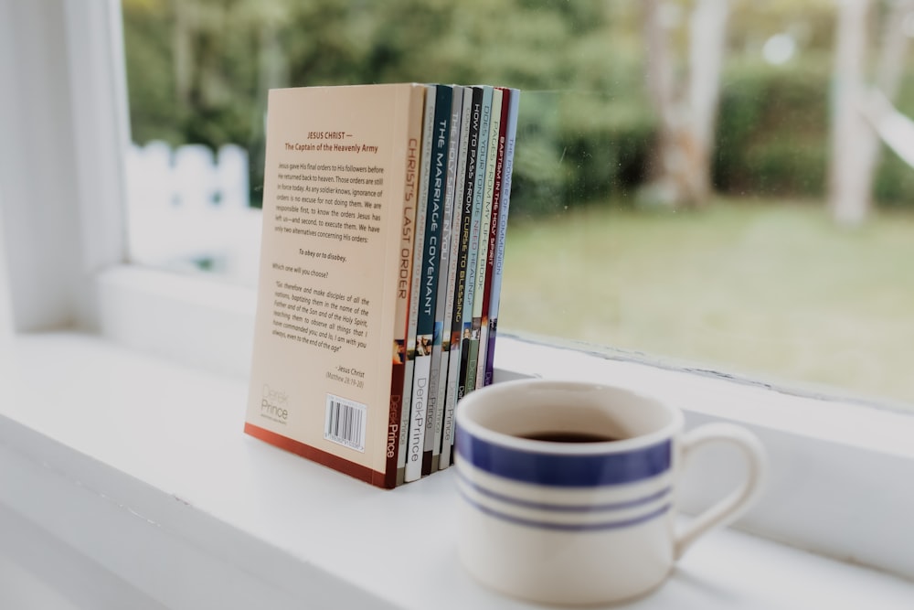 Ein Stapel Bücher auf einer Fensterbank neben einer Tasse