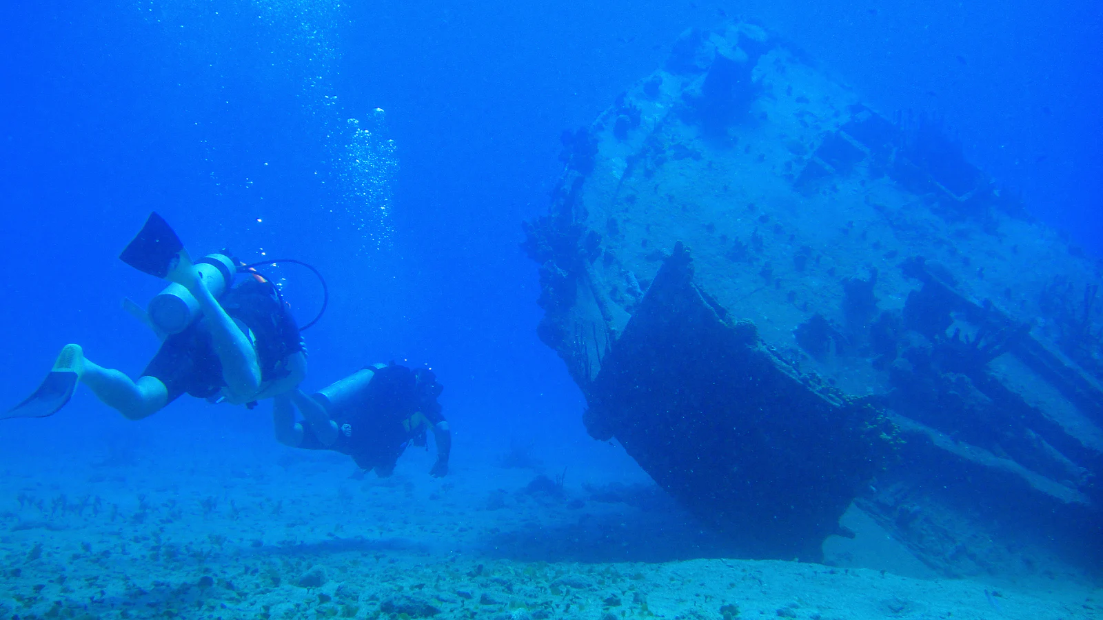 Two scuba divers approaching a sunken shipwreck on the sand