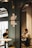 In a modern cafe setting, two people are seated across from each other, each focused on their devices. A stylish emblem is mounted on a dark-colored partition wall, with industrial-style lighting enhancing the ambiance.