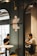 In a modern cafe setting, two people are seated across from each other, each focused on their devices. A stylish emblem is mounted on a dark-colored partition wall, with industrial-style lighting enhancing the ambiance.