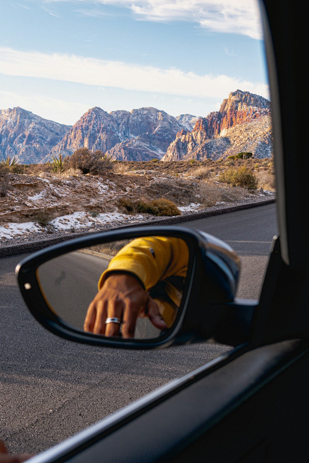 a person taking a picture of mountains in a rear view mirror