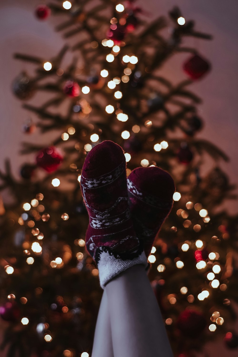 a person's feet wearing mittens in front of a christmas tree