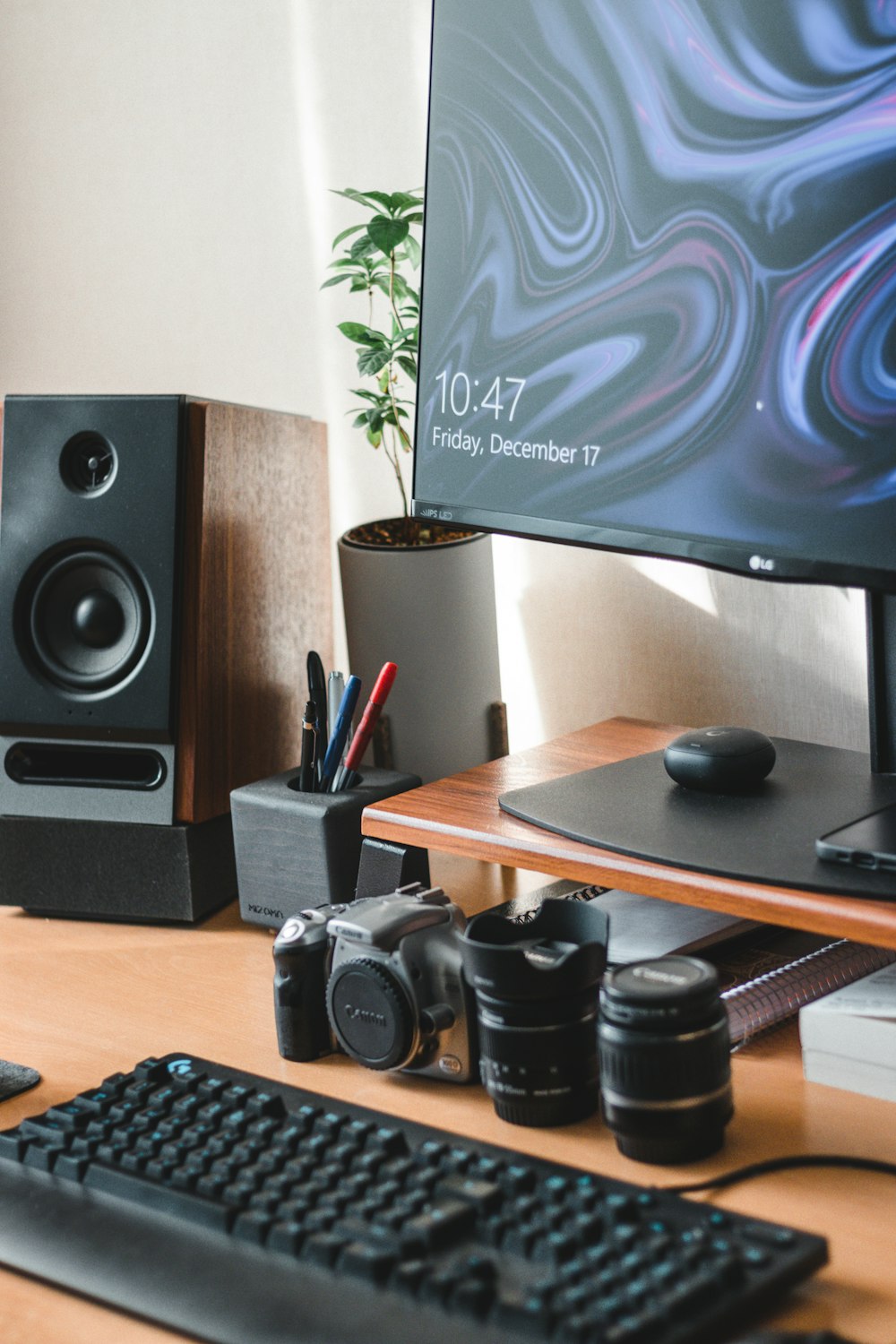 a desk with a keyboard, monitor, speakers and a plant