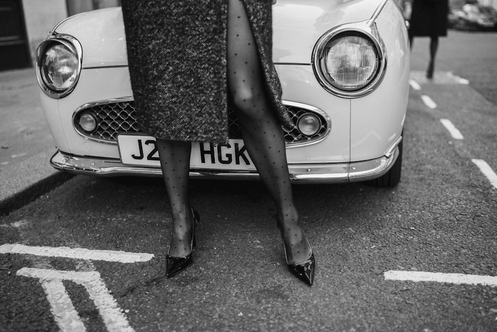 a black and white photo of a woman leaning on a car