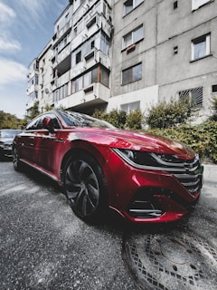 A shiny red compact car parked near a vibrant urban market street