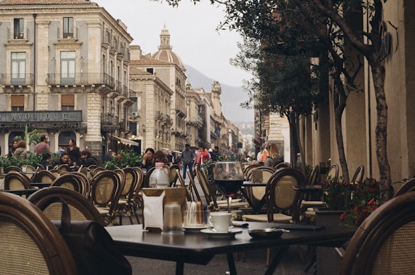 A lively European café terrace with people enjoying coffee surrounded by cobblestone streets and old architecture.