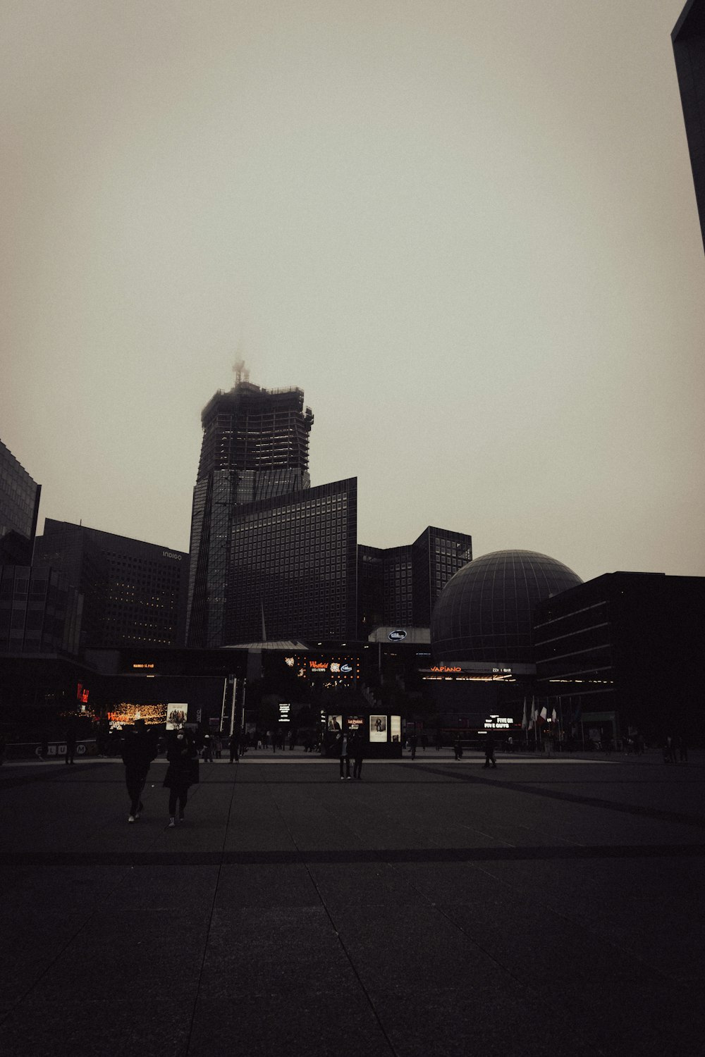 a group of people walking across a street next to tall buildings