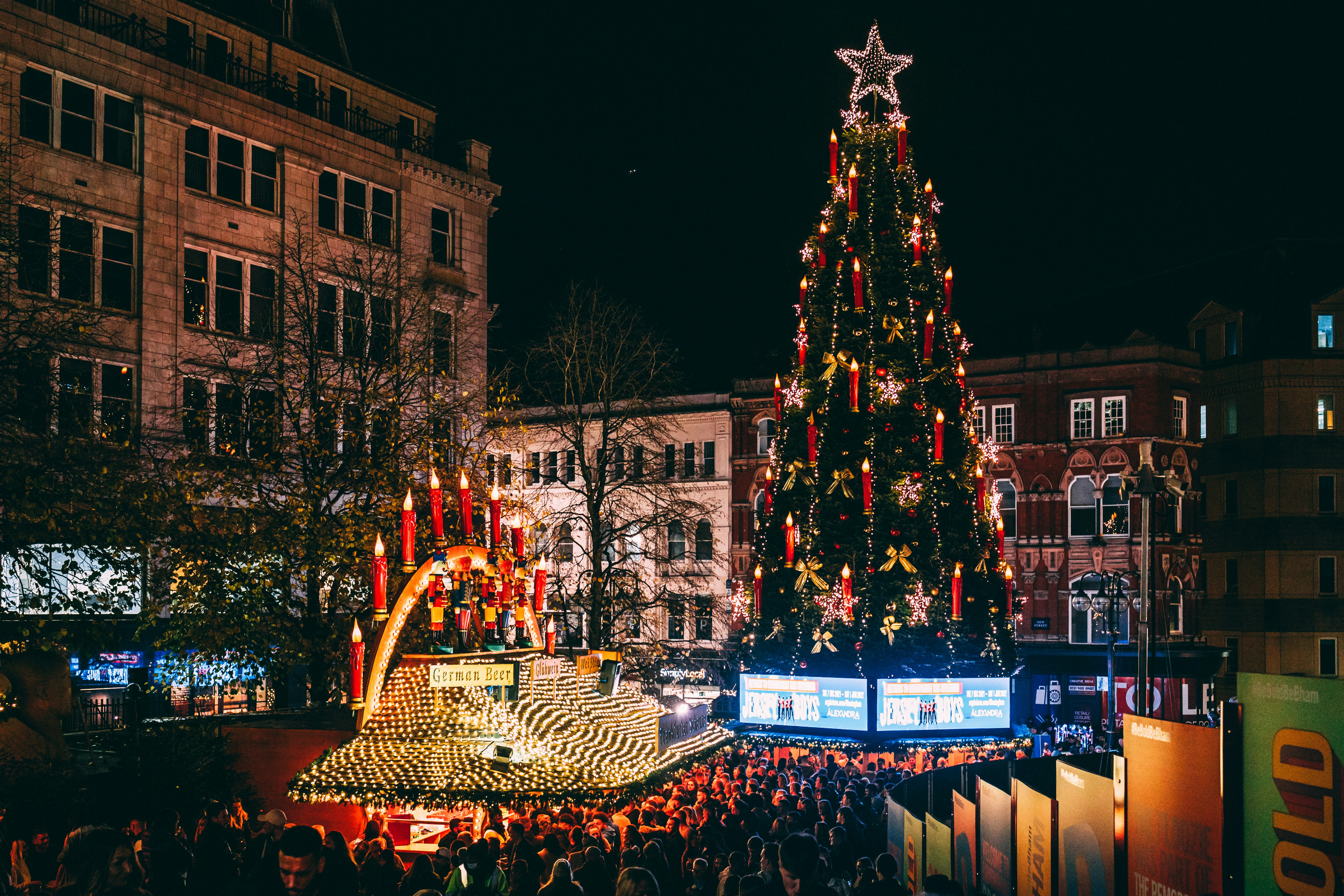 a large christmas tree is lit up in the middle of a crowded street