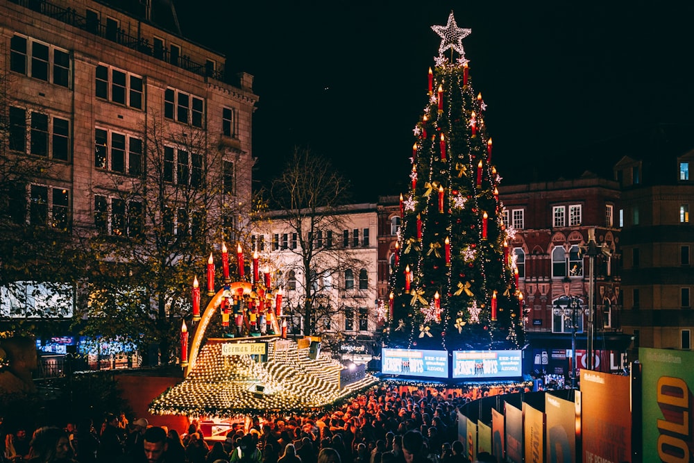 a large christmas tree is lit up in the middle of a crowded street