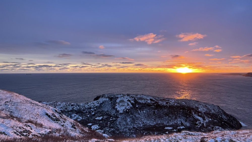 the sun is setting over the ocean on a snowy day