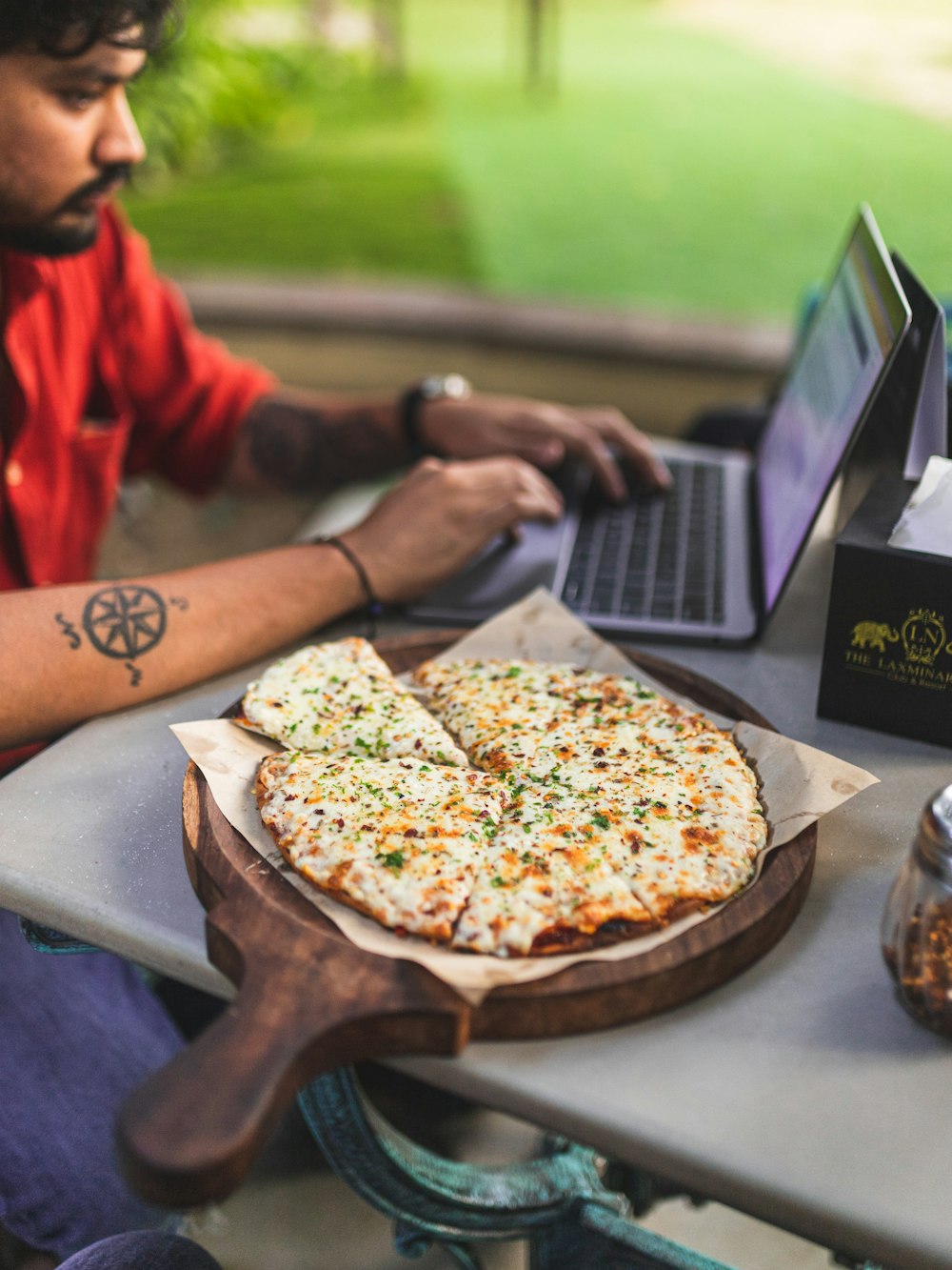 a man sitting at a table with a pizza and a laptop