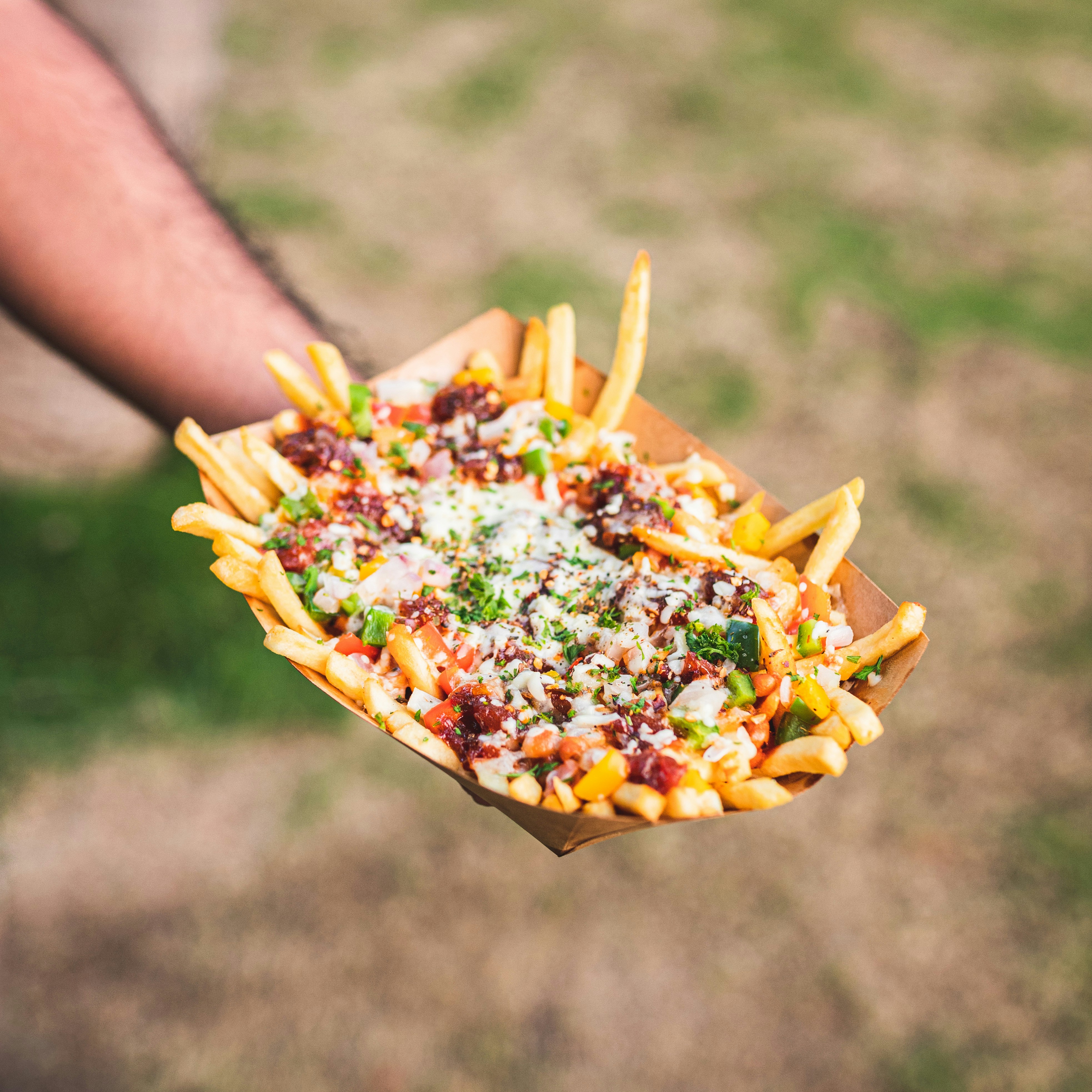 a person holding a tray of fries with bacon and cheese and other toppings