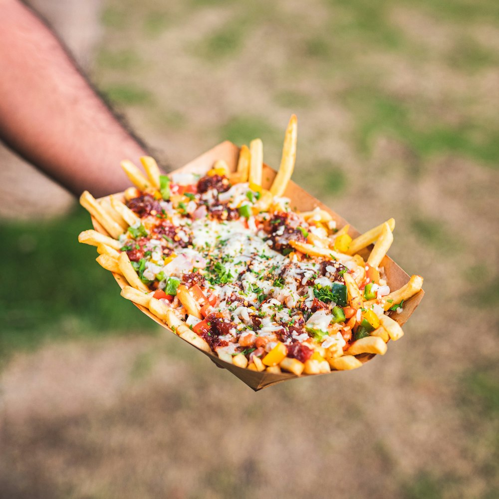 a person holding a tray of fries with cheese and other toppings