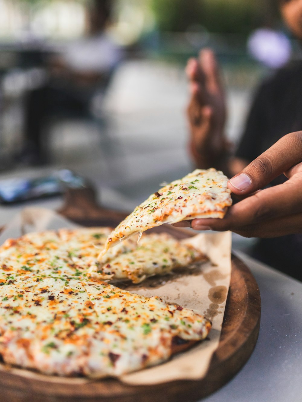 a person taking a slice of pizza from a wooden platter