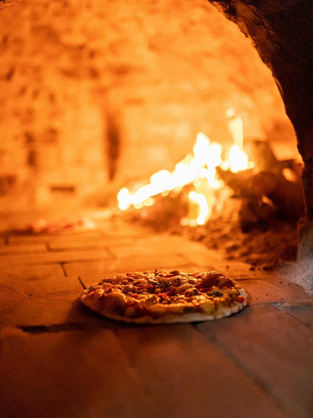 a pizza sitting in front of a fire in a brick oven