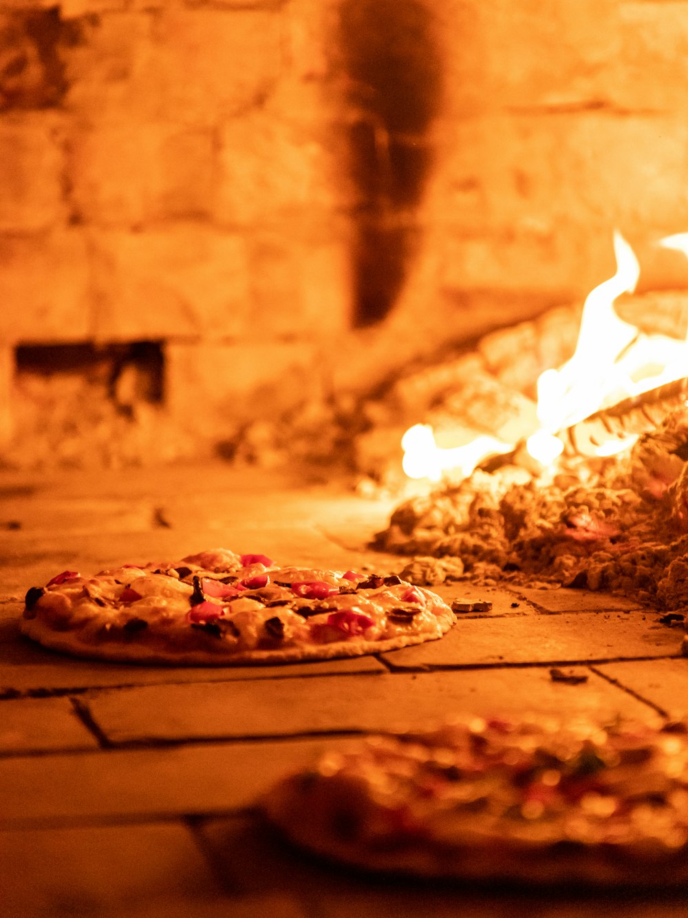 two pizzas sitting on the floor in front of a fire