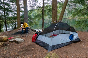 A peaceful campsite setup with a small fire and tents surrounded by tall pine trees