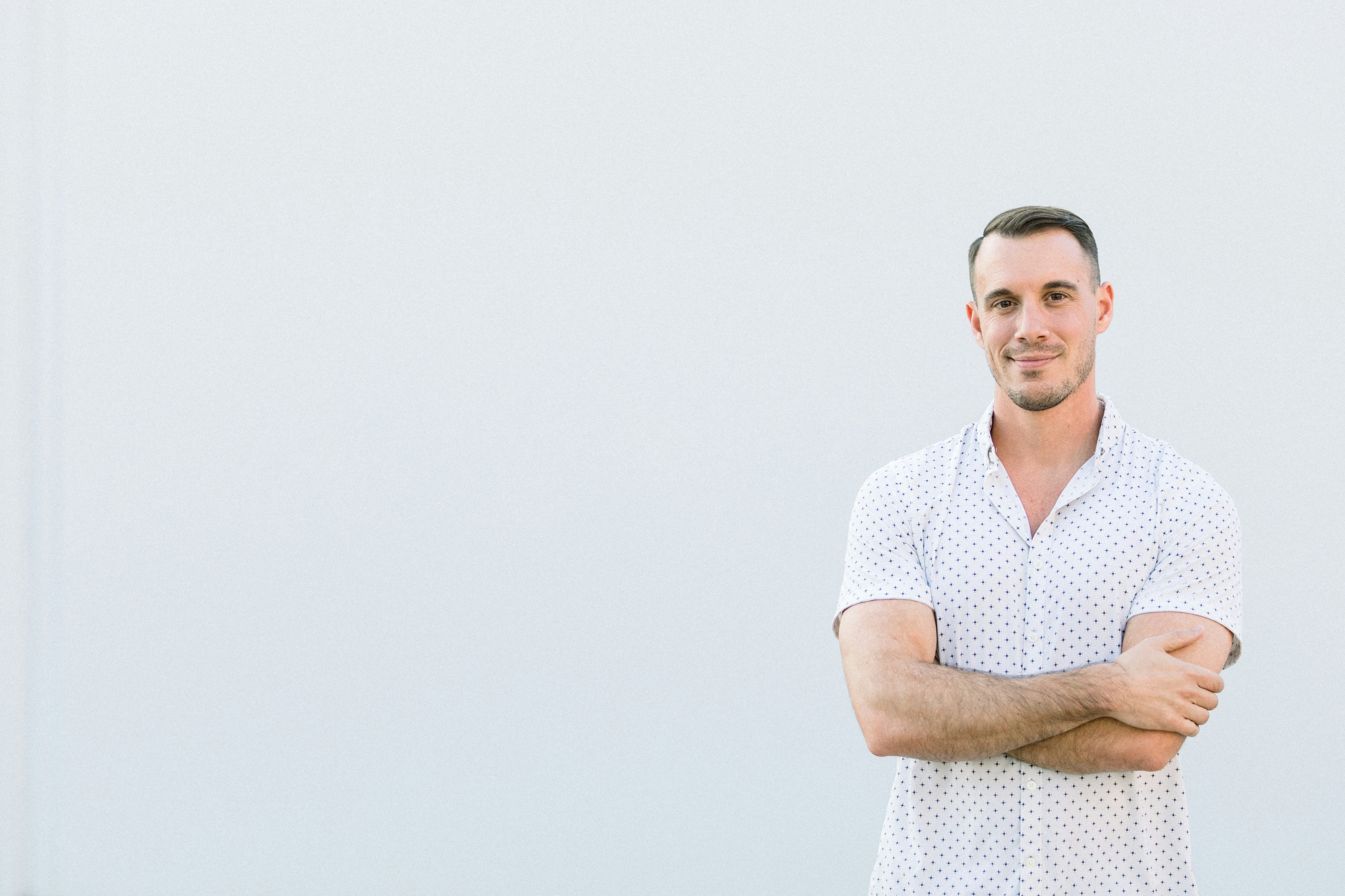 Alex Sanfilippo, the founder of PodPros, confidently stands alone with arms crossed in front of a white wall. Model Alex Sanfilippo, the founder of PodMatch.com