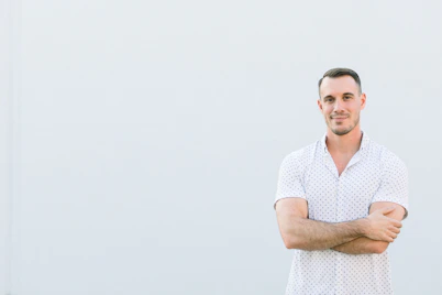 a man standing with his arms crossed in front of a white wall