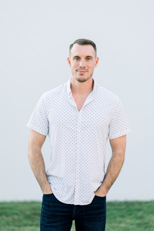 A man dressed in a modern casual shirt and jeans, standing relaxed against a neutral background.