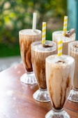 Variety of milkshake flavors lined up in clear glasses with fresh fruit garnishes.