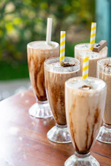 Two tall glasses of creamy shakes topped with chocolate and nuts, set on a cozy café table.