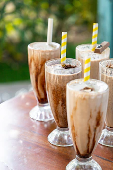 Two tall glasses of creamy shakes topped with chocolate and nuts, set on a cozy café table.