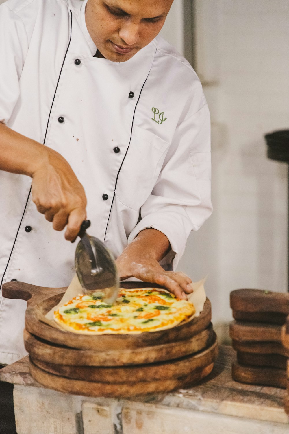 a man cutting a pizza on top of a wooden table