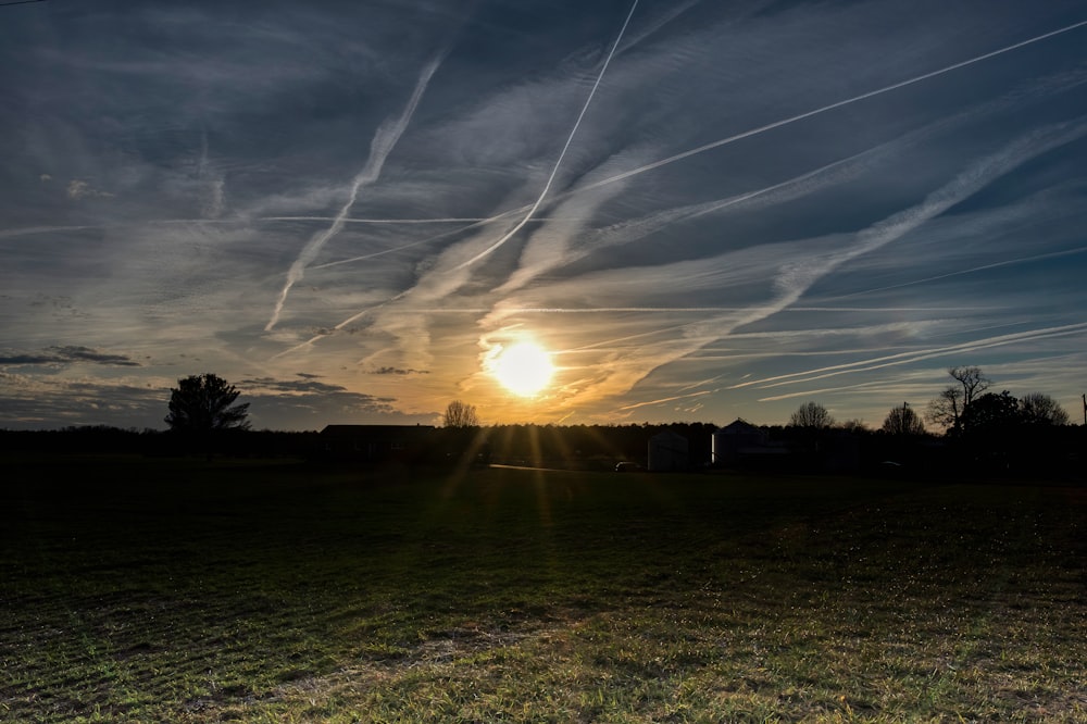 the sun is setting over a field with contrails in the sky