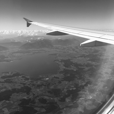 A vibrant airplane soaring above a patchwork of green mountains and blue lakes.