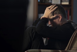 a man sitting on a couch holding his head in his hands