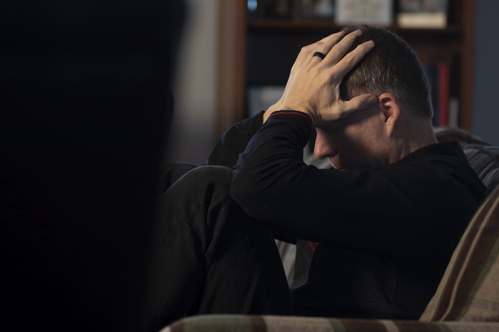 a man sitting on a couch holding his head in his hands