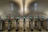 A modern transportation terminal with a series of turnstiles lined up under an architecturally designed ceiling with smooth, curved lines. The turnstiles have digital displays and card readers. Surrounding signs indicate exit only and closed platforms.