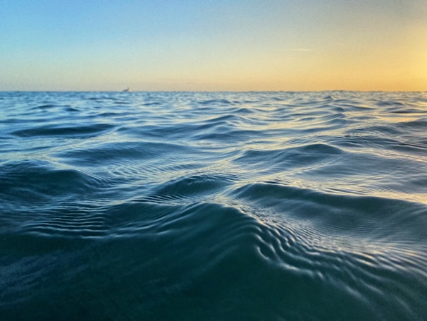 A calm ocean horizon at golden hour, evoking the peaceful feeling of a beach day.