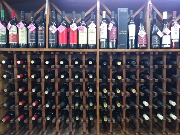 Close-up of a rustic wooden wine rack filled with various Greek wine bottles at Ampelos.