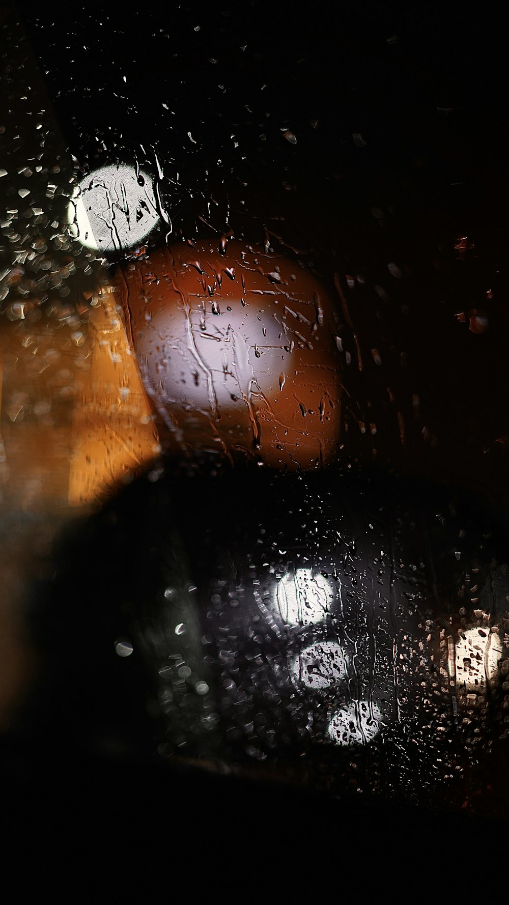 a close up of a rain covered window with a traffic light in the background