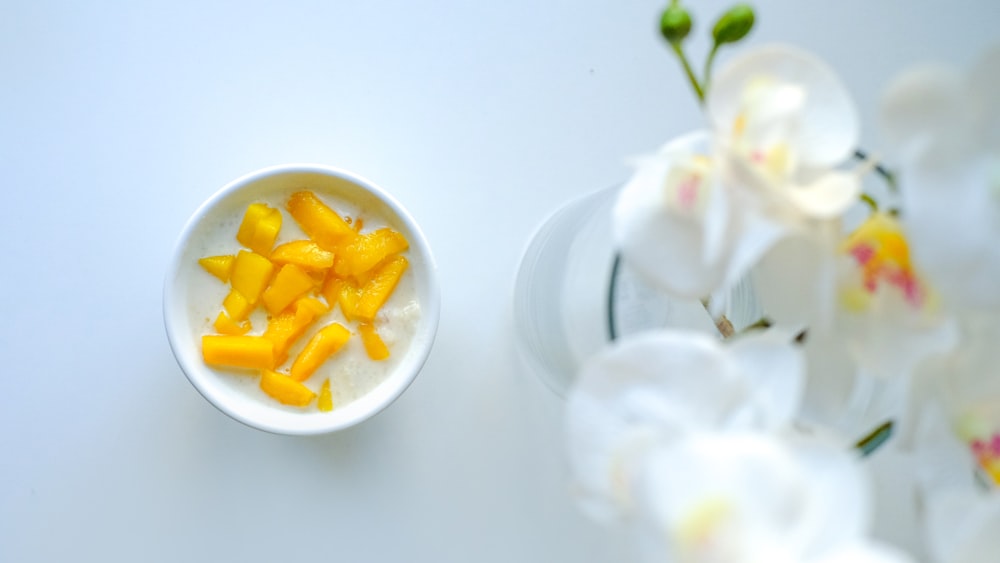 a white bowl filled with fruit next to white flowers